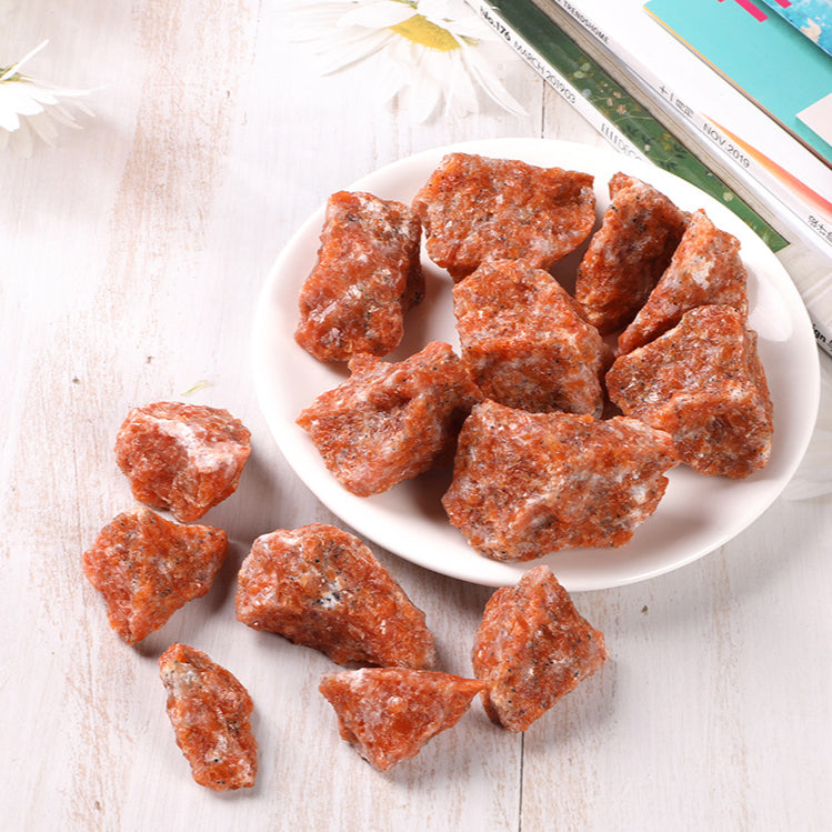  A close-up of a natural rough sunstone, displaying its warm orange and gold hues with shimmering inclusions that catch the light, highlighting its vibrant and energizing qualities.